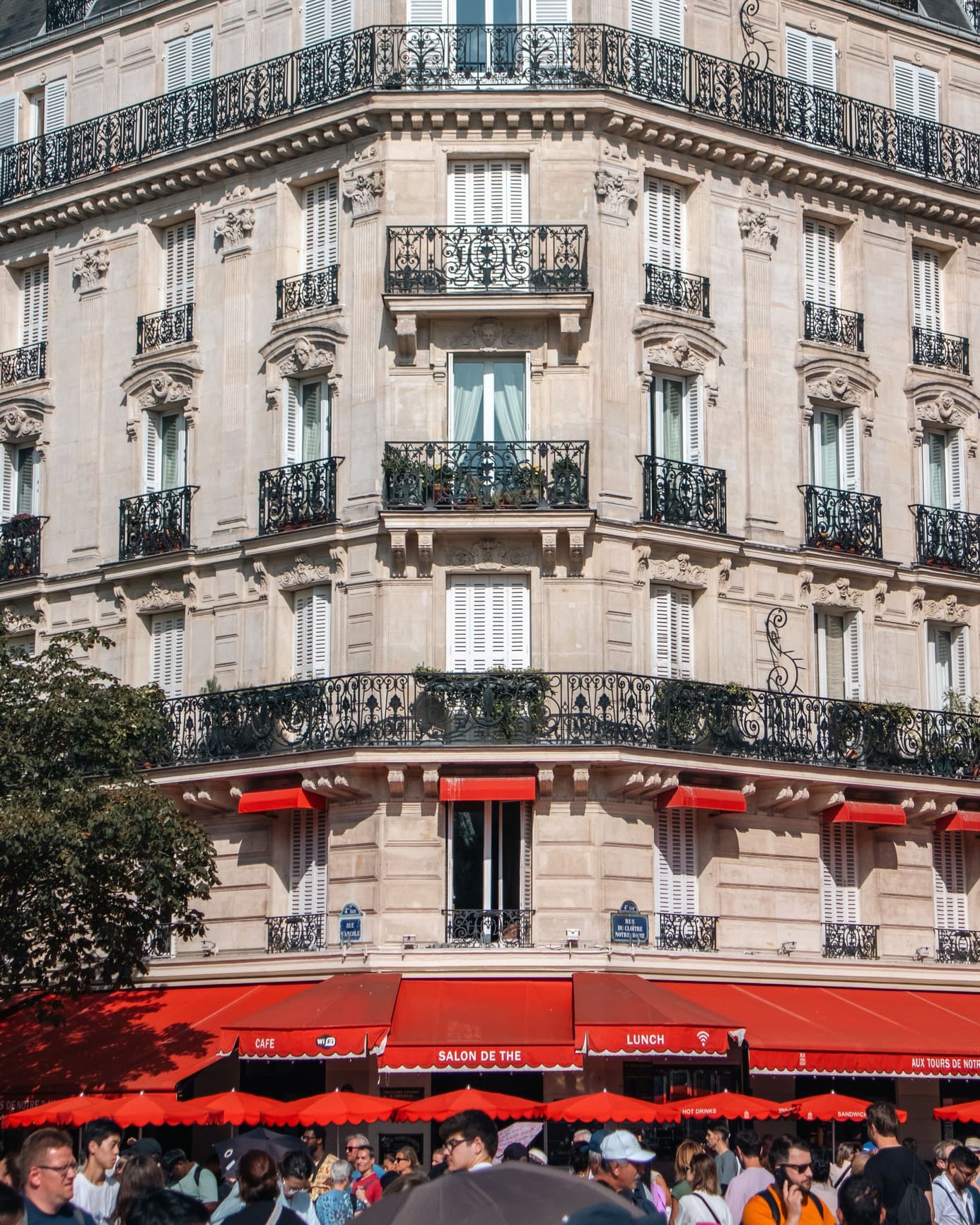 Immeuble haussmannien à balcons en fer forgé, passants devant les terrasses au pied de la façade